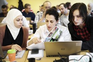 Three students discussing something in front of a laptop computer. 